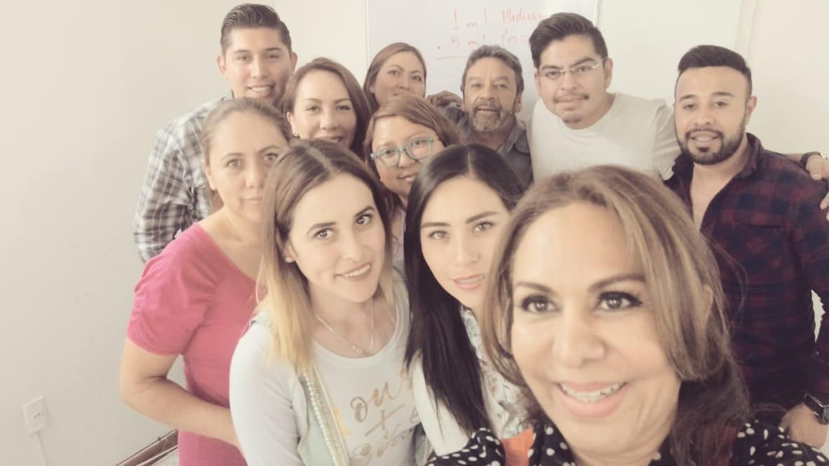 Grupo de alumnos y docentes sonriendo en el aula, frente al pizarrón